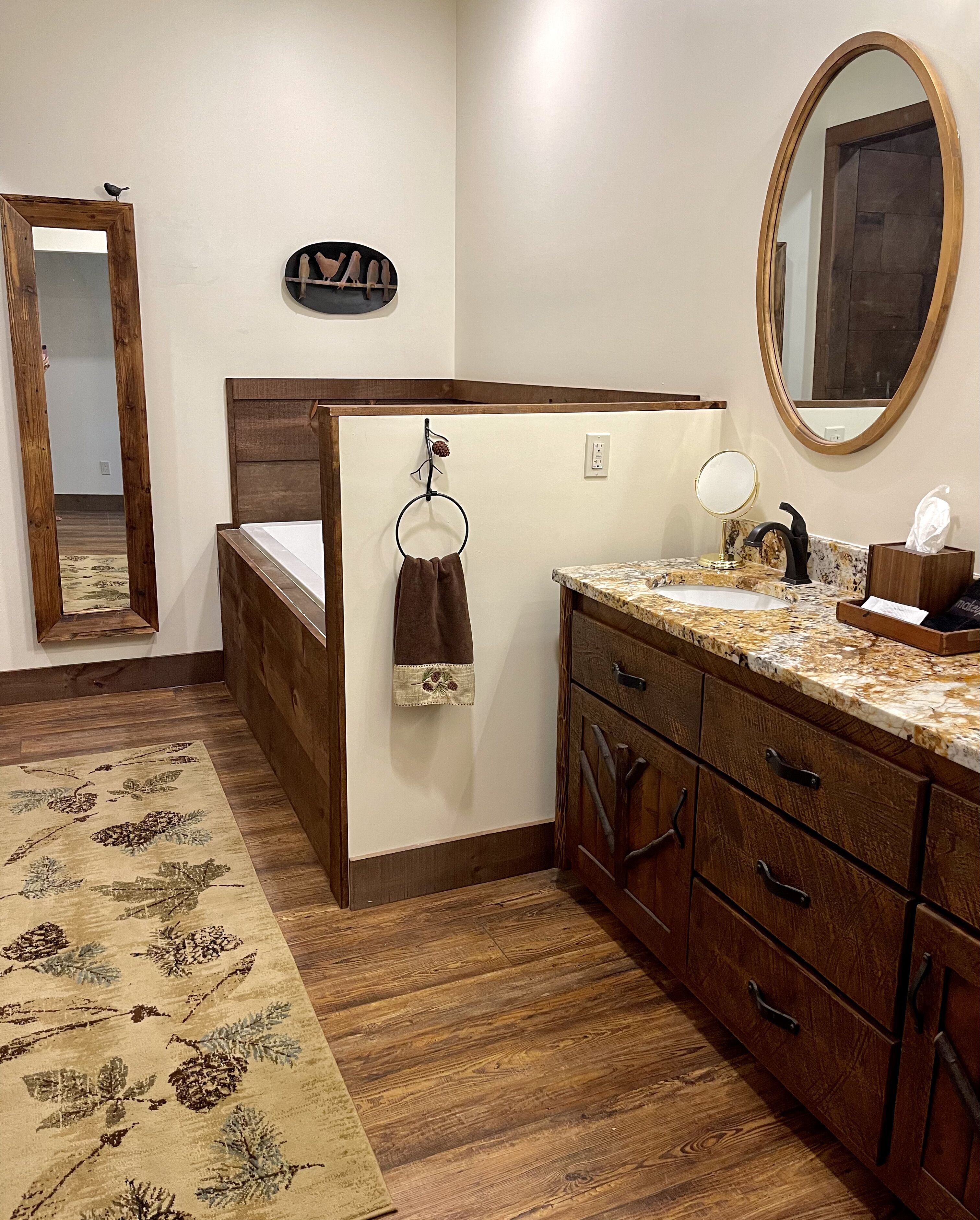 A bedroom with a wooden bed, a wooden dresser, a bathroom vanity, and a mirror.