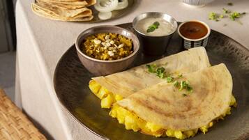 A table with a plate of food including a folded flatbread, a bowl of curry, and a bowl of yogurt.