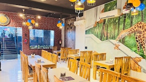 A restaurant with wooden tables and chairs, a brick wall, and a mural of a giraffe. - Qotel Comfort Chattarpur- Near Chattarpur Metro (New Delhi)