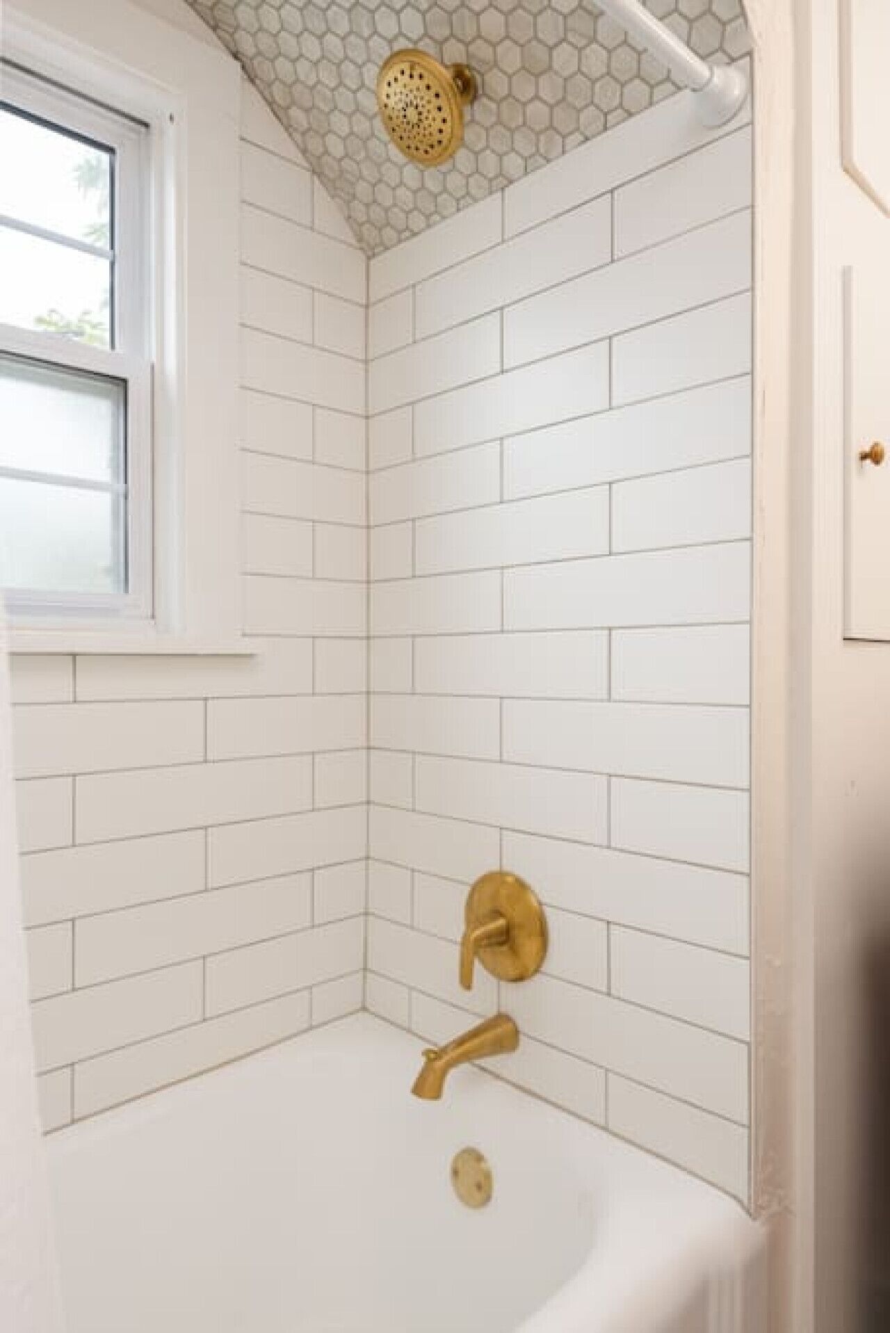 Ein Badezimmer mit weißen Fliesen im U-Bahn-Stil, einem goldfarbenen Duschkopf und einem Wasserhahn aus Gold.