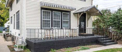 A two-story house with a front porch, a black railing, and a small front yard.