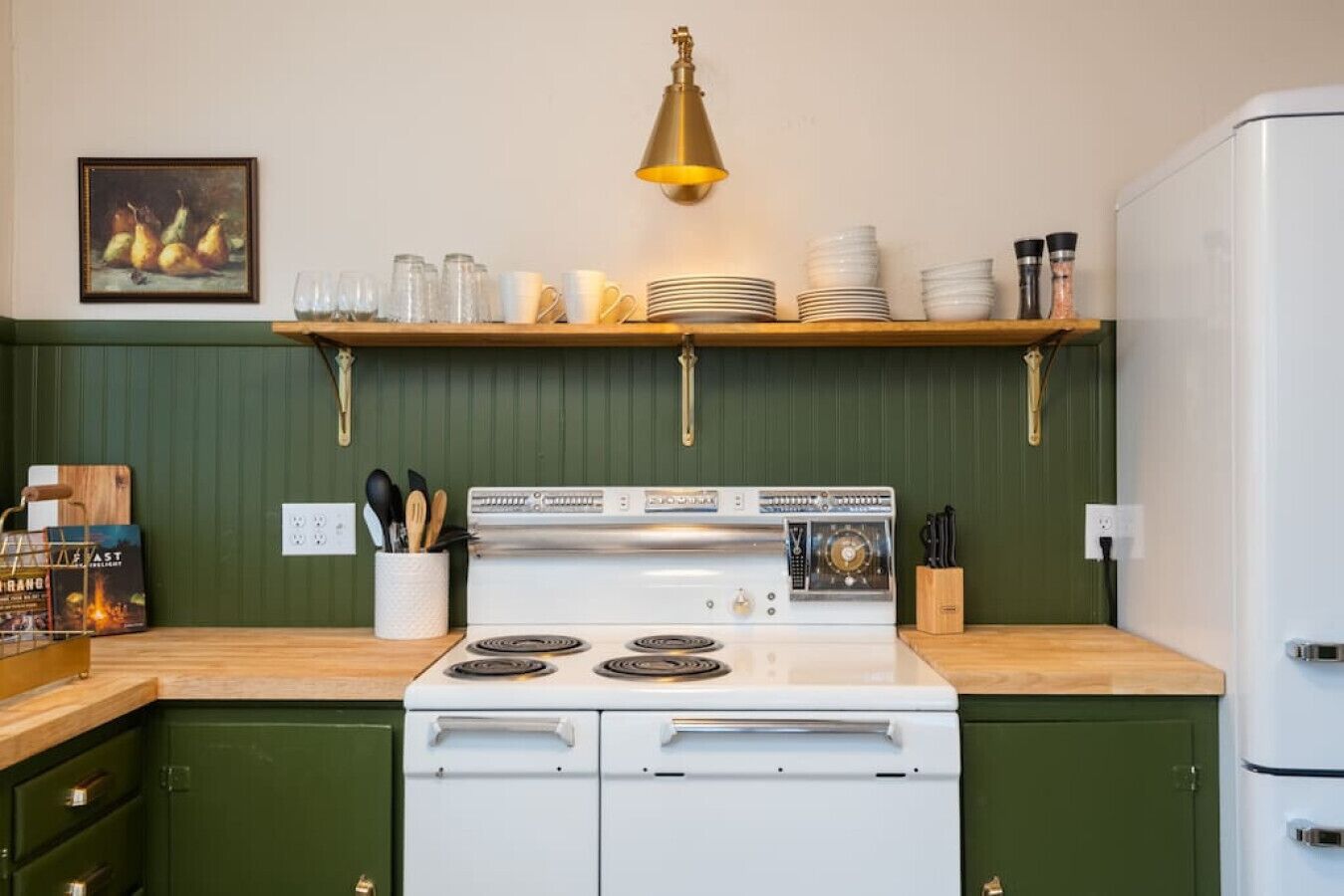 A kitchen with a white stove, green cabinets, a wooden countertop, and a hanging light fixture.