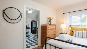 Een slaapkamer met een bed, een dressoir, een nachtkastje, een lamp en een raam met jaloezieën.