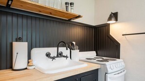 Een keuken met een witte spoelbak, zwarte kastjes, een fornuis en een houten aanrecht.