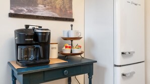 Une petite cuisine équipée d’une machine à café Keurig, d’une tasse à café, d’un plateau avec des en-cas et d’un réfrigérateur blanc.