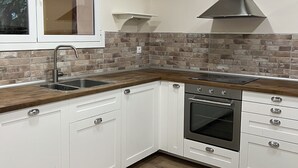 Een moderne keuken met witte kasten, een roestvrijstalen afzuigkap, een tegelwand van baksteen en een houten aanrecht.