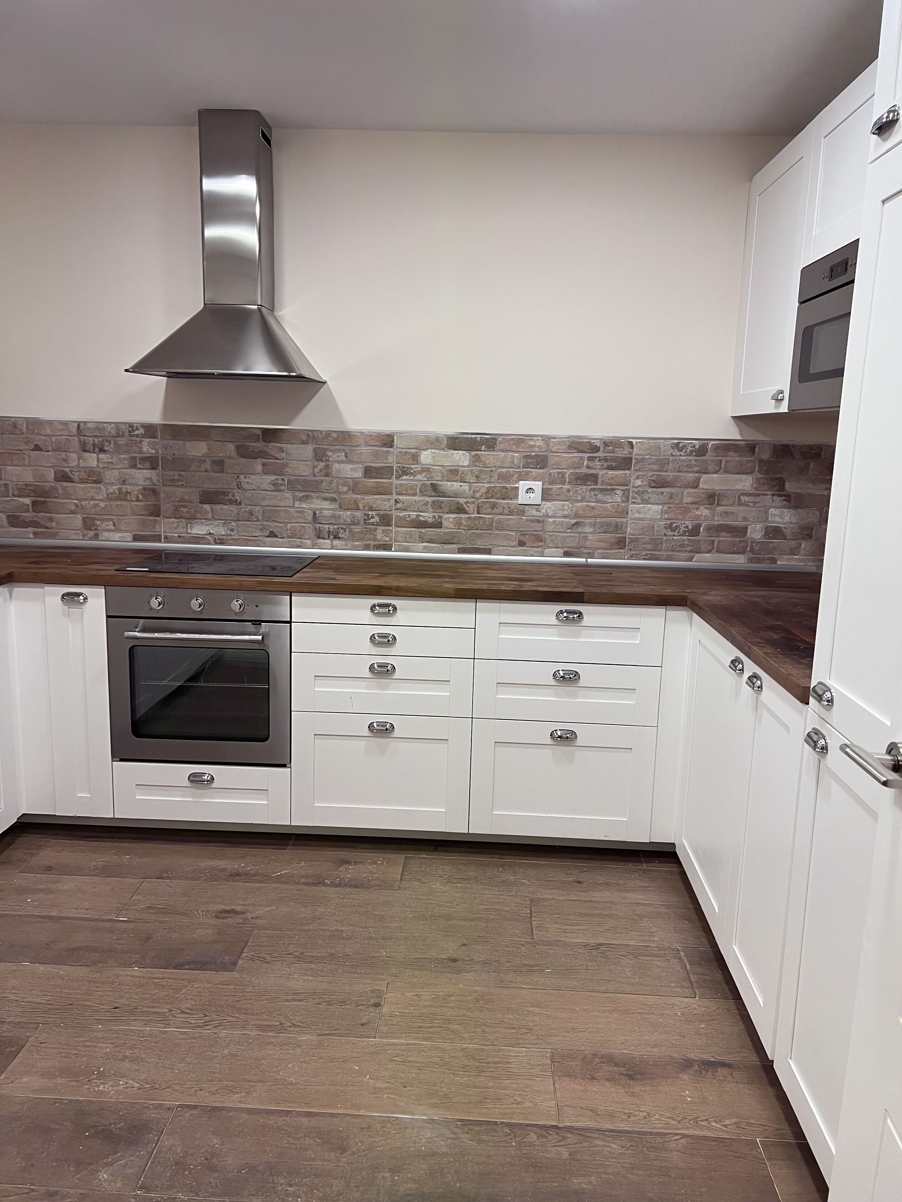 Una cocina con gabinetes blancos, extractor de acero inoxidable, salpicadero de ladrillo y microondas.