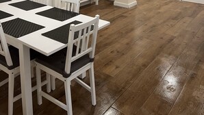 Een ruime kamer met een grote witte tafel en stoelen, een flatscreen televisie aan de muur en een houten vloer.