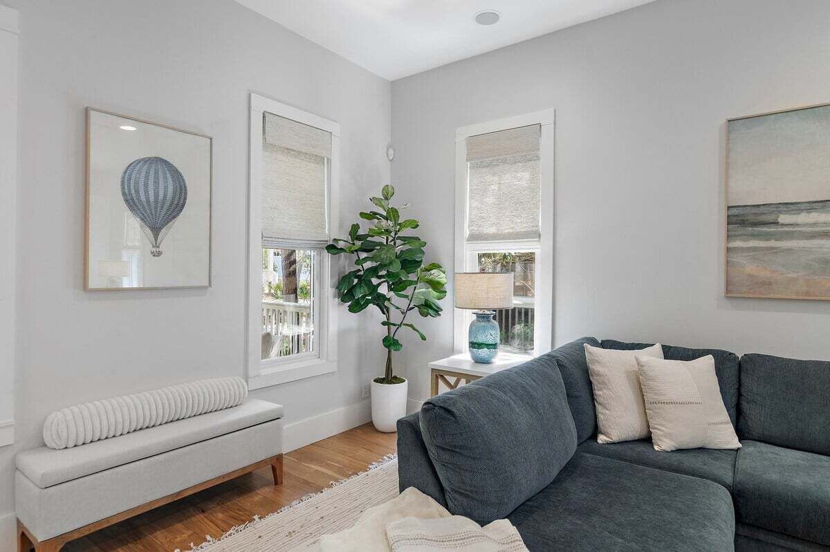 Un salón con un sofá gris, un banco blanco y una planta grande en maceta.