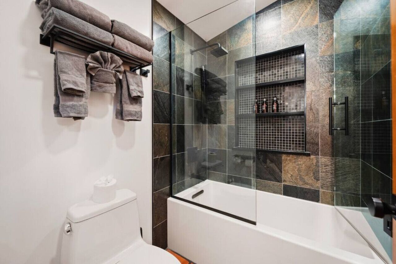 A modern bathroom with a glass-enclosed shower, a white bathtub, and a towel rack with folded towels.