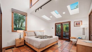 Ein Schlafzimmer mit Bett, Schreibtisch, Stuhl und einem Fenster mit Blick auf Bäume.