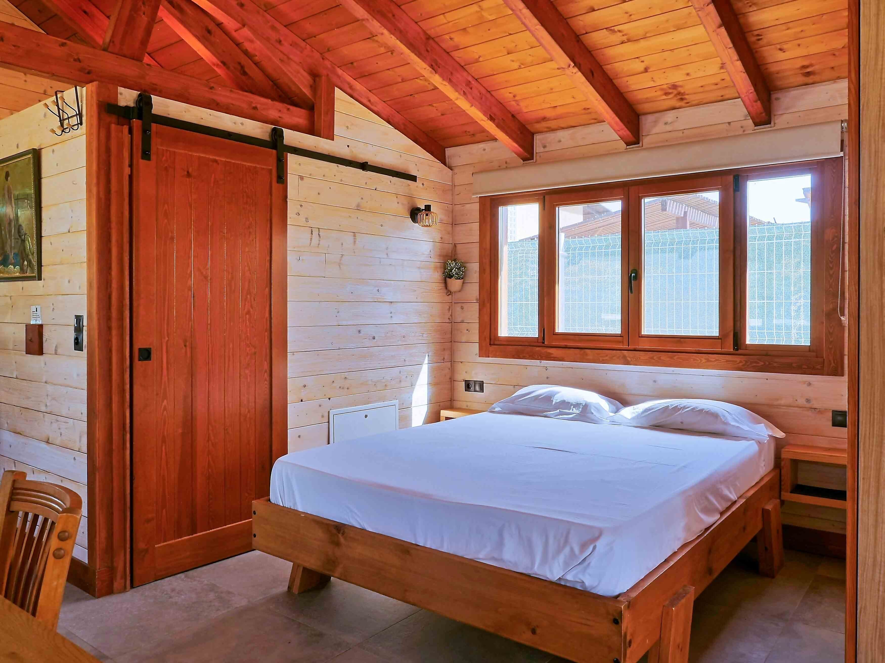 Een kamer met houten wanden, een bed, een schuifdeur en een raam.