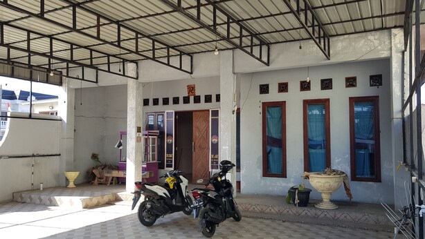 A covered parking area with two motorcycles parked, a tiled floor, and a building entrance with windows and a door. - Hotel O Cempaka Syariah (Medan)