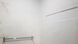 A corner of a room with a white wall, a metal towel rack, and a visible patch of wall damage. - Hotel O Cempaka Syariah (Medan)