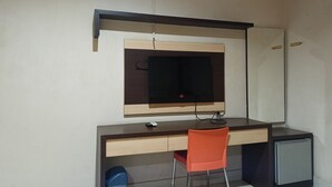 A compact room with a desk, a chair, a television, and a small refrigerator. - Collection O 93163 Hotel Grand Kartika (Makassar)