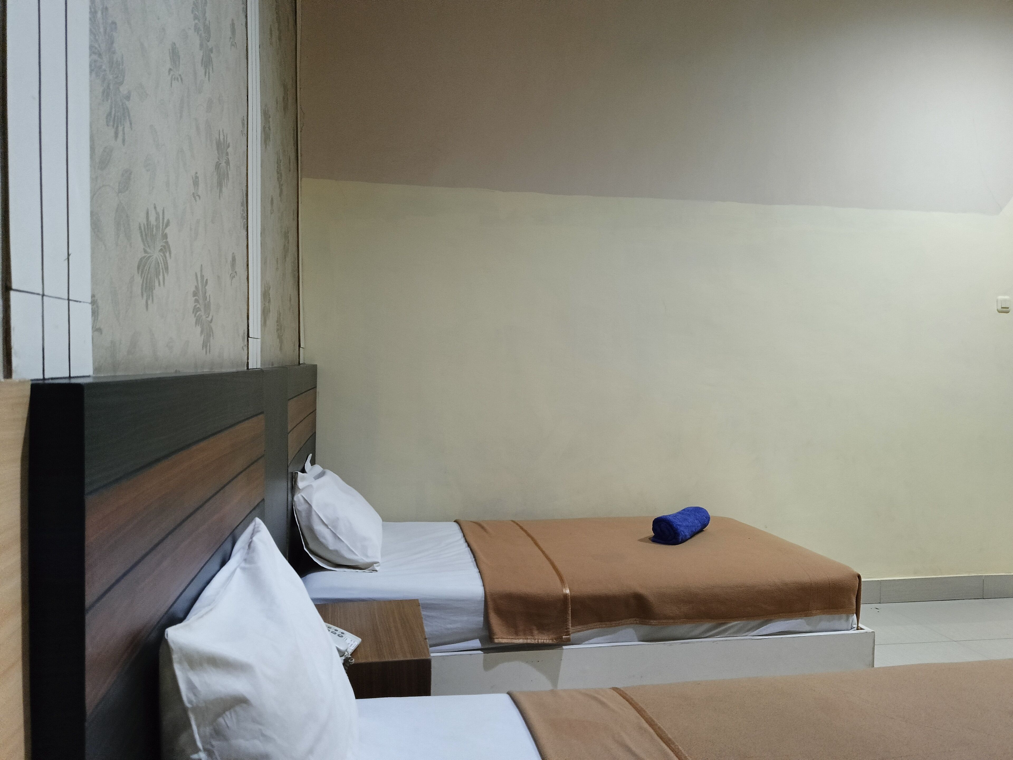 A hotel room with two beds, a wooden headboard, a nightstand, and a wall with a floral pattern.
