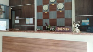 A reception area with a checkered wall design, multiple clocks, and a reception sign. - Collection O 93163 Hotel Grand Kartika (Makassar)