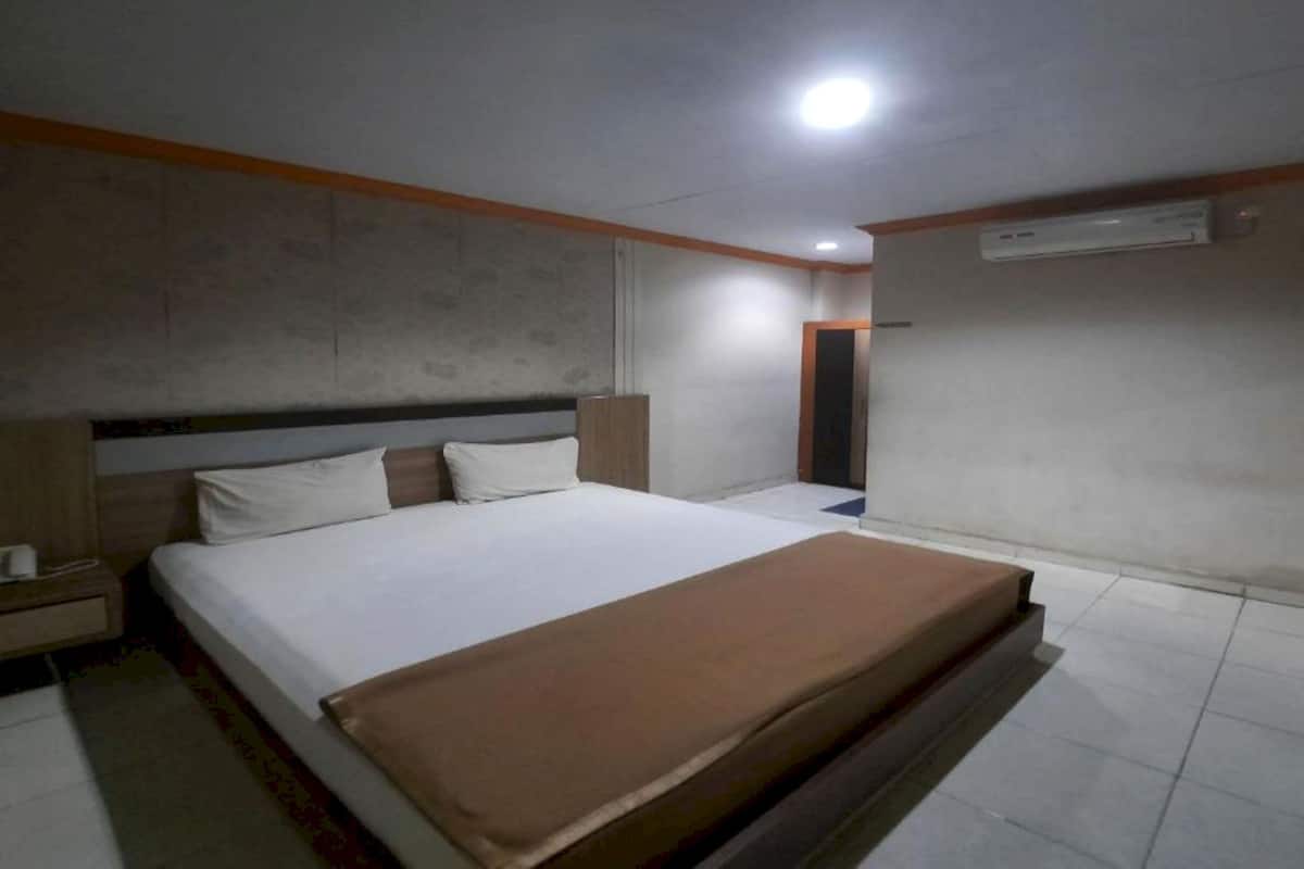 A bedroom with a bed, nightstand, and an air conditioning unit on the wall.