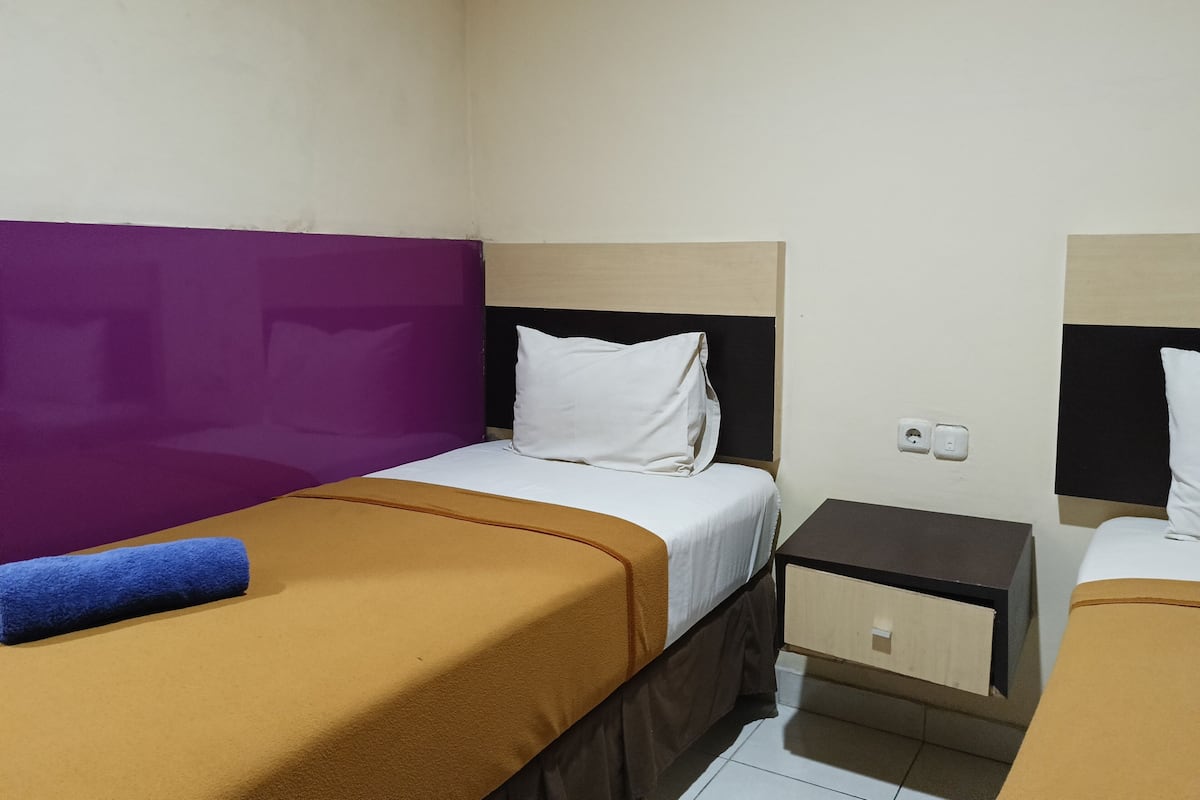 A hotel room with two single beds, each with a distinct color headboard, a small bedside table, and a power outlet.