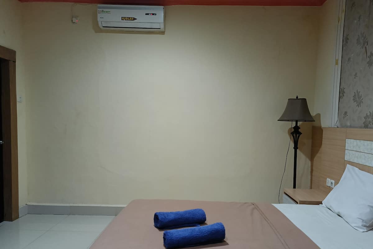 A hotel room with a bed, a nightstand, a lamp, and an air conditioning unit on the wall.