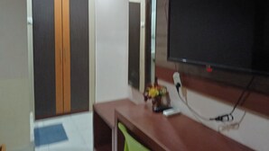 A room with a television mounted on the wall, a wooden desk, and a door with vertical stripes. - Collection O 93163 Hotel Grand Kartika (Makassar)