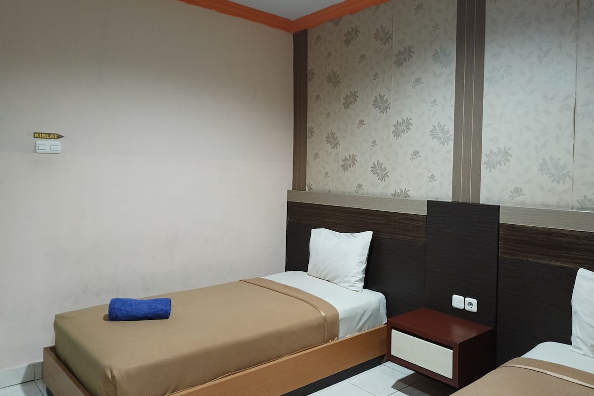 A hotel room with two single beds, a nightstand, a small table, and a wall-mounted shelf.