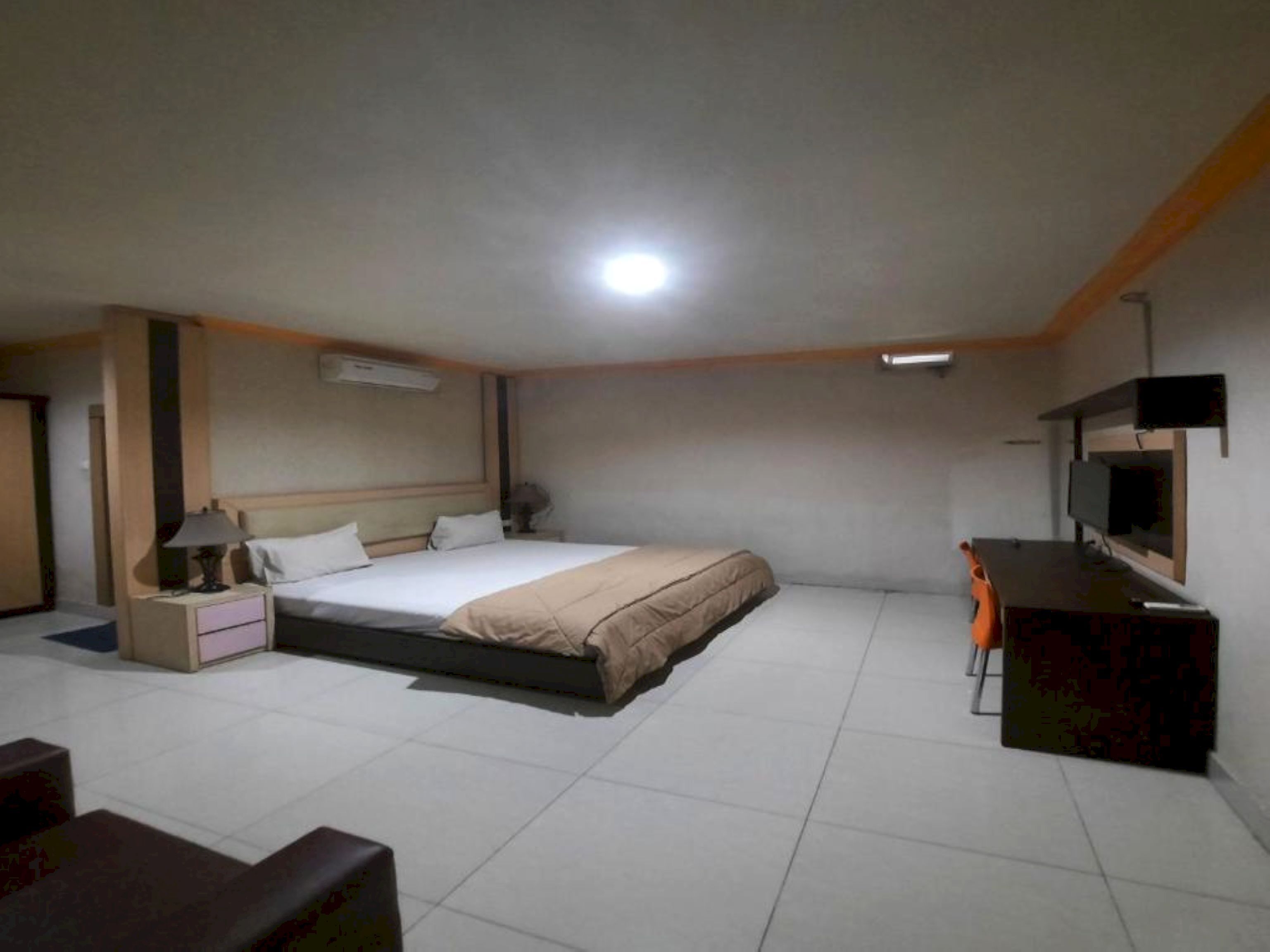 Een hotelkamer met een bed, nachtkastje, lamp en een bureau met stoel.