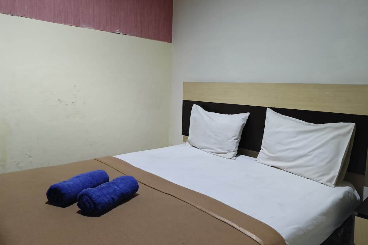A hotel room with a bed, two pillows, and two rolled towels.