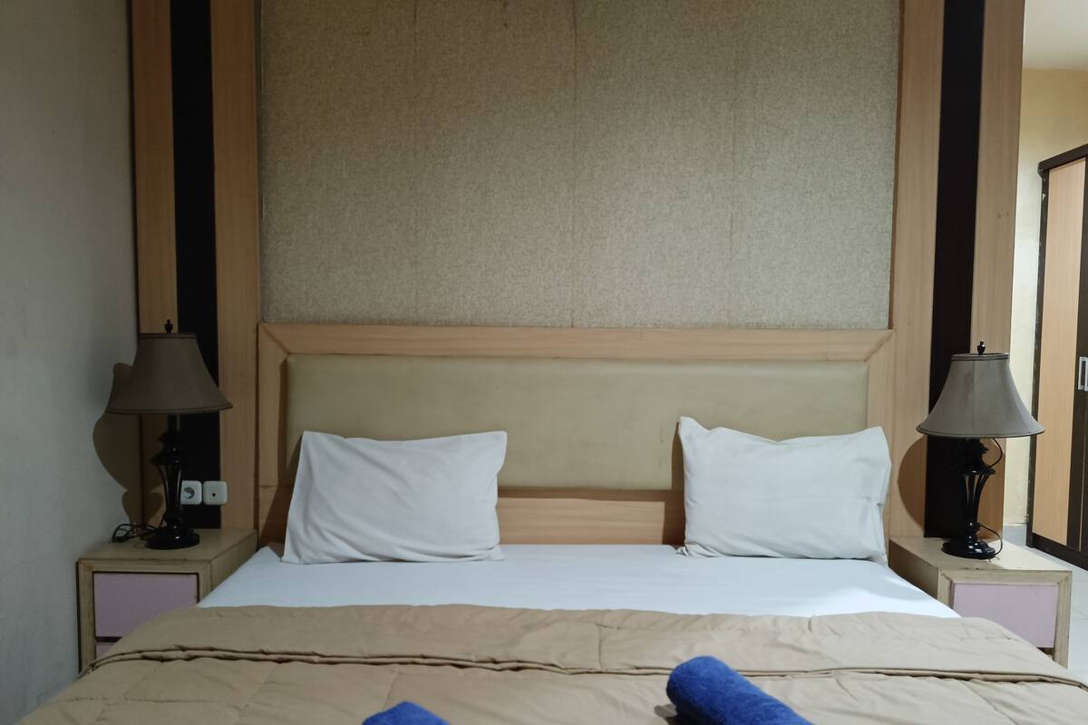 A hotel room with a large bed, two bedside lamps, and a headboard.