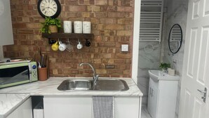 A kitchen with a brick wall, a sink, a microwave, and a coffee machine. - Nice And Cosy Large Studio Near Luton Airport! (Luton)