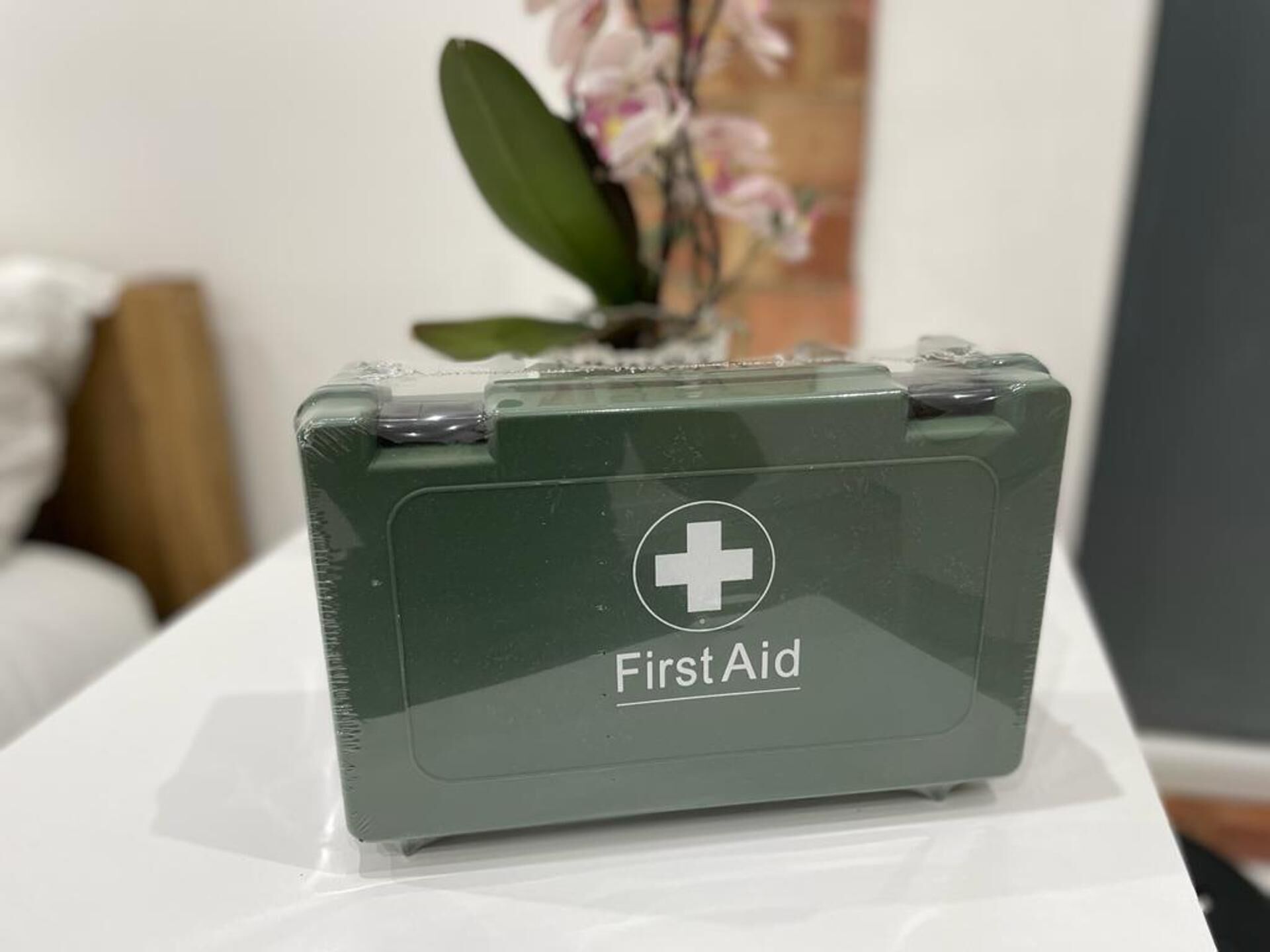 A green first aid kit on a white surface with a plant in the background.