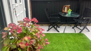 A patio with a round table and four chairs, a small potted plant, and a green artificial turf. - Nice And Cosy Large Studio Near Luton Airport! (Luton)