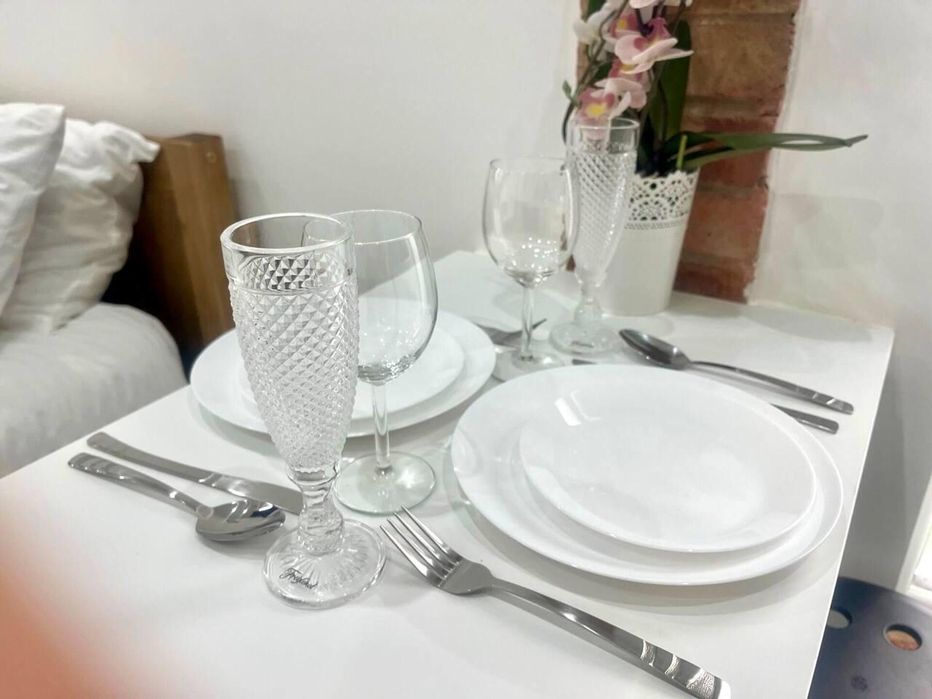 A dining table set with white plates, cutlery, and crystal glasses.