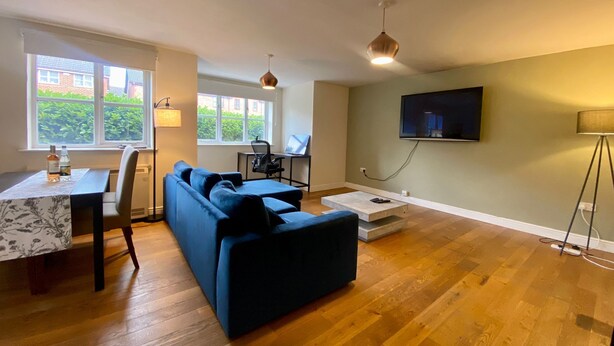 Un soggiorno moderno con un divano, un tavolo da pranzo, una TV a parete e un'ampia finestra con vista sul verde.