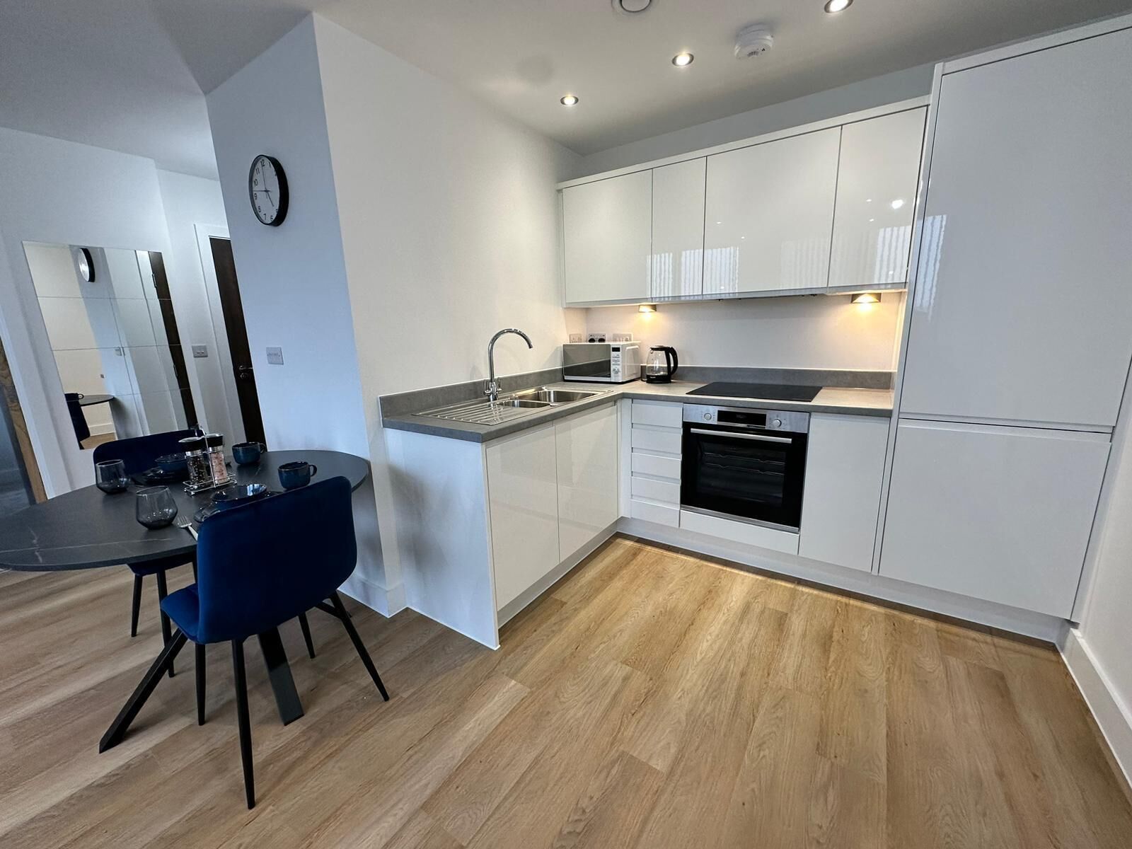 Eine moderne Küche mit weißen Schränken, einem eingebauten Backofen und einem Essbereich mit Tisch und Stühlen.