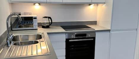 Une cuisine moderne avec des meubles blancs, un évier en acier inoxydable, une bouilloire et un four encastré.
