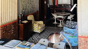 Une pièce avec un papier peint à motifs, une lanterne rouge suspendue, une table à manger avec des chaises, et une petite table avec des livres et une lampe.
