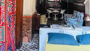 Une pièce avec un lit, une table avec des livres, une lampe rouge suspendue et un rideau à motifs.