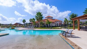 A swimming pool with lounge chairs, palm trees, and a building with a red roof in the background. - Century Stone Hill North (Pflugerville)