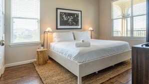 A bedroom with a bed, two bedside lamps, a framed picture on the wall, and a wooden side table. - Century Stone Hill North (Pflugerville)