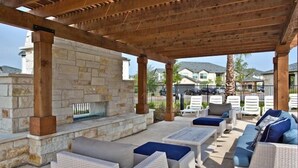 An outdoor patio area with stone walls, wicker furniture, and a grill. - Century Stone Hill North (Pflugerville)