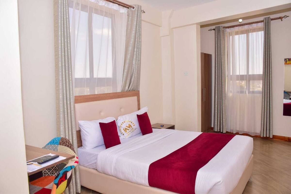 Quarto de hotel com uma cama, mesa de cabeceira, escrivaninha e guarda-roupa.