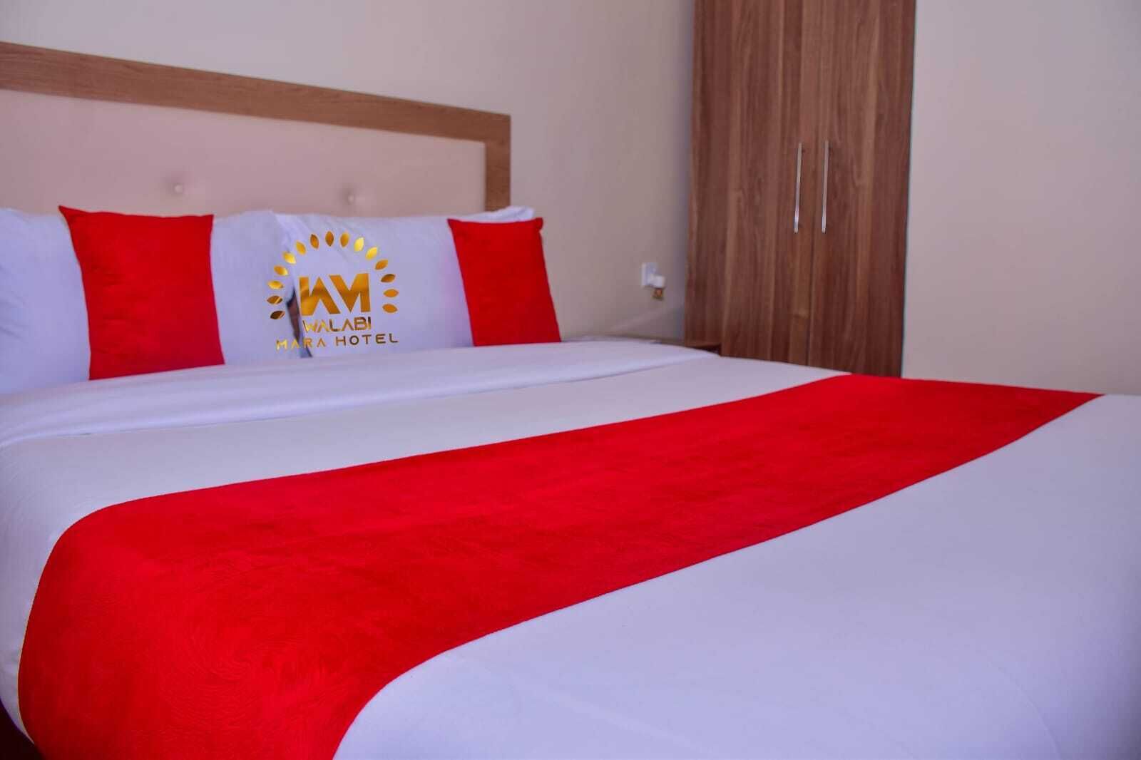 A hotel room with a bed, red and white bedding, and a logo on the headboard.