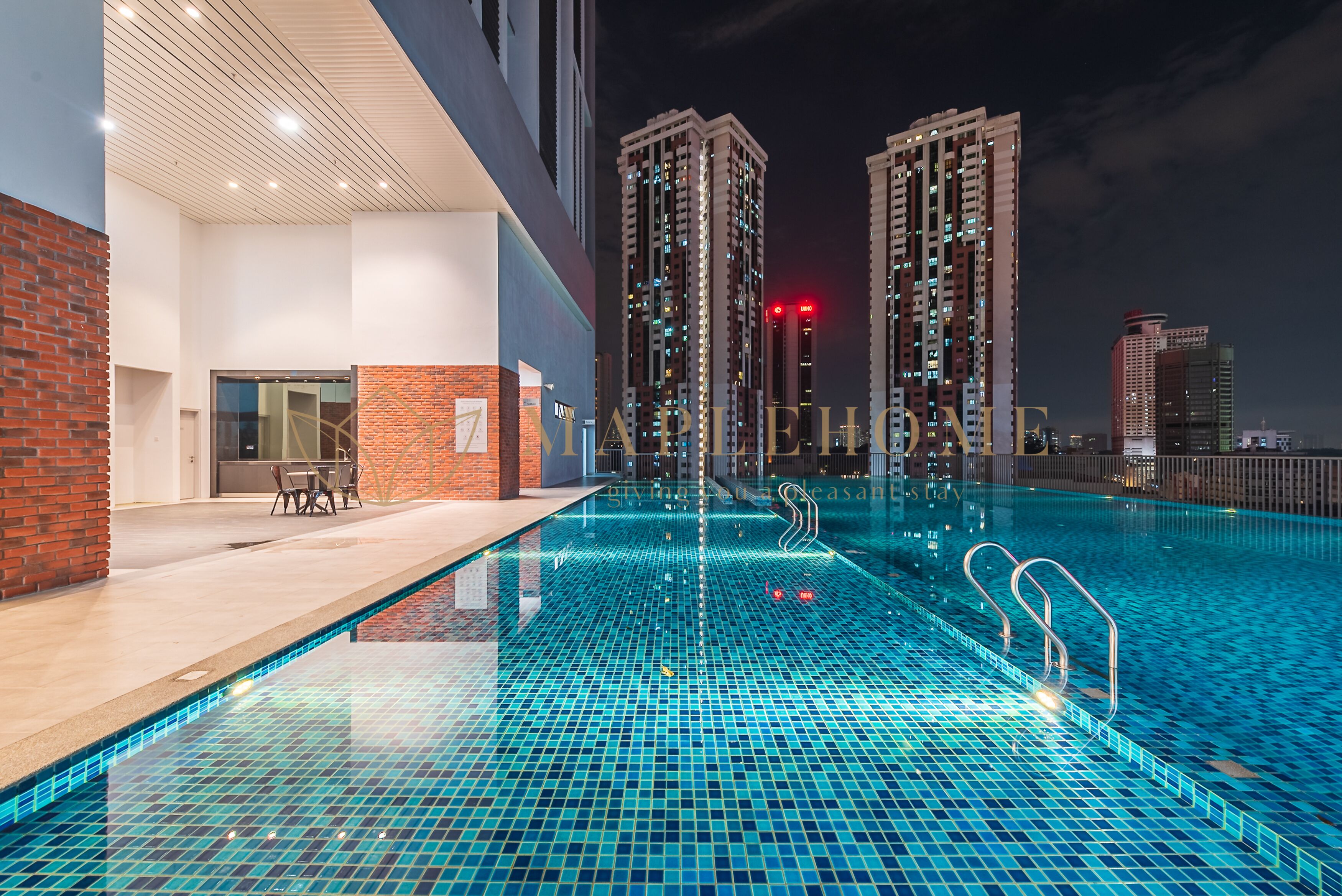 Una piscina en la azotea con piso de baldosas, rodeada de edificios altos y un muro de ladrillo.