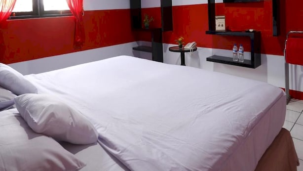 A hotel room with a large bed, a bedside table with a phone and water bottles, and a red and white color scheme. - Hotel O Permata Ria Hotel (Manado)