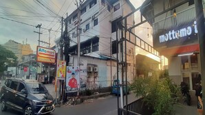 A street view with a black car parked on the side, a sign for Alfamart, and a building with a sign that reads "nottomo". - Hotel O Permata Ria Hotel (Manado)