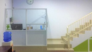 A room with a staircase, a water dispenser, a clock, and a desk with a computer. - OYO 93169 Bnb Homestay  (Makassar)