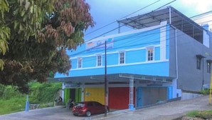 A two-story building with a blue and grey facade, a red car parked in front, and a tree to the left. - OYO 93169 Bnb Homestay  (Makassar)