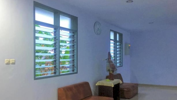 A room with a brown leather sofa, a small table with a vase, and two windows with blinds. - OYO 93169 Bnb Homestay  (Makassar)
