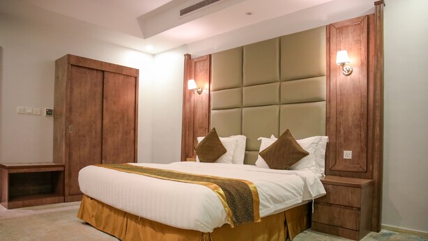 A bedroom with a large bed, wooden headboard, two nightstands, and a wardrobe. - Areen palace hotel (Jeddah)